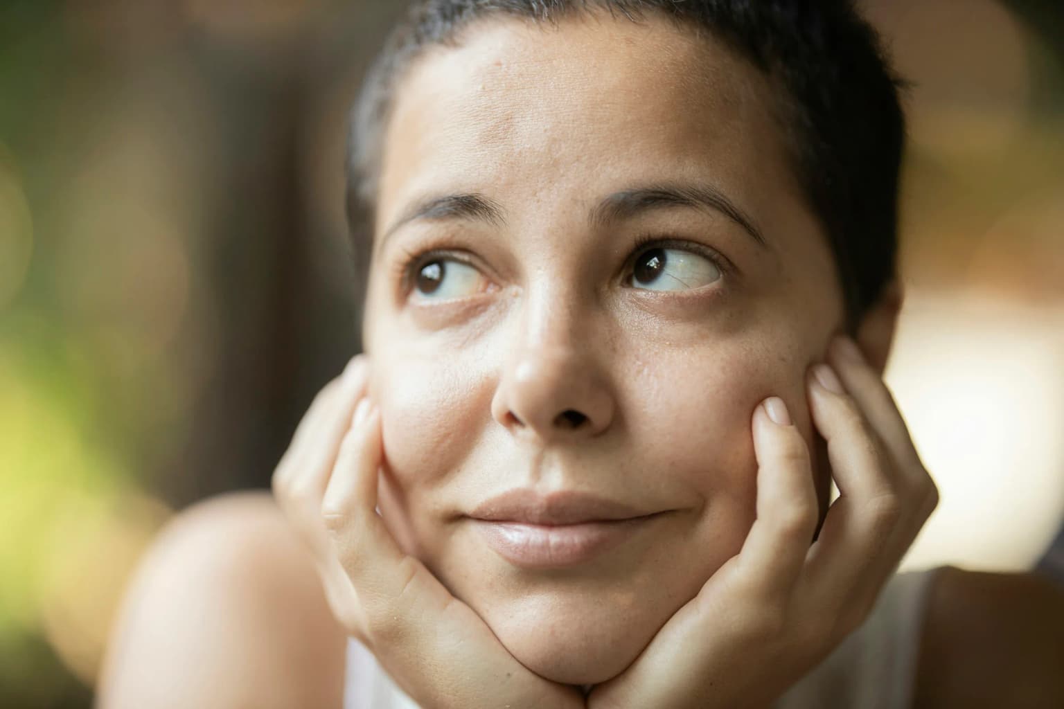 Mujer sonriente con las manos en las mejillas, piel hidratada.