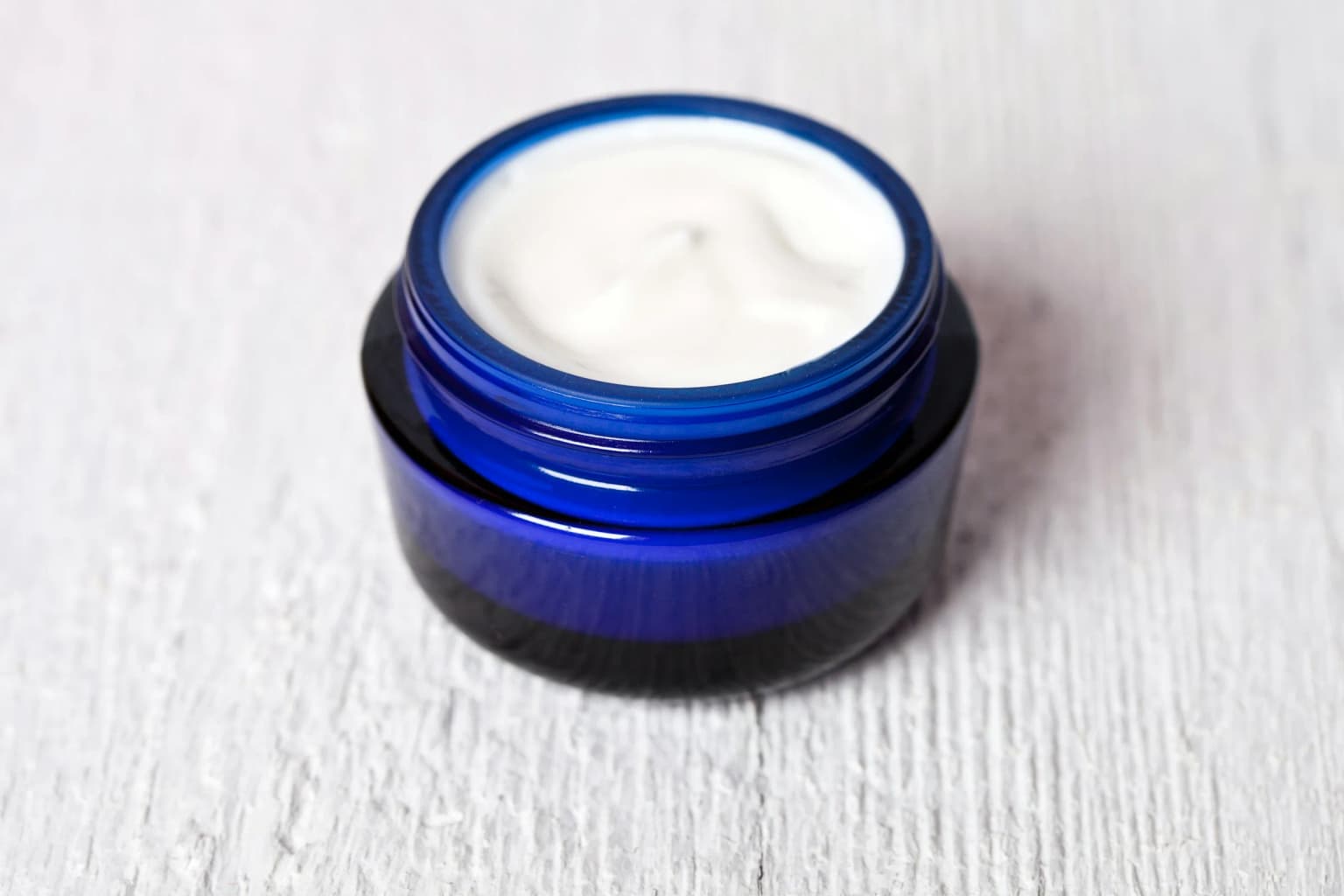 Frasco de crema facial abierto sobre una superficie clara.