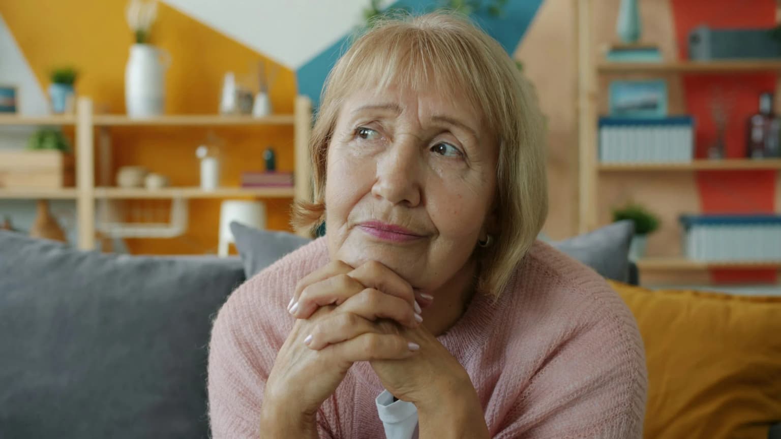 Mujer pensativa sentada en el sofá con la mirada perdida.