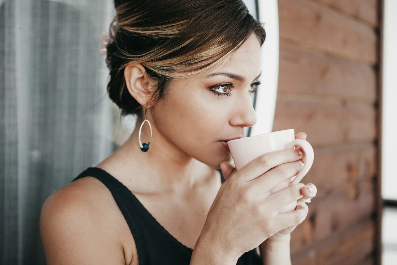 Mujer pensativa con una taza de café junto a la ventana.